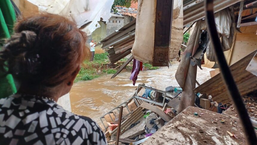 Pemilik bengkel 'Cibubur Jaya Motor' Herti, 66, syok usai kejadian longsor dialaminya, duit dan tasnya terseret aliran Kali Baru di Jalan Raya Bogor Km 27, No 4, Cibubur, Jakarta Timur, Senin (26/2) siang. Foto: Joesvicar Iqbal/ipol.id